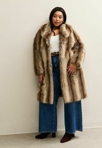 Faux-Fur-Mantel in braunen und beigen Streifen mit lockerer Passform. Kombiniert mit hoch geschnittenen Schlagjeans und dunklen Ankle Boots.