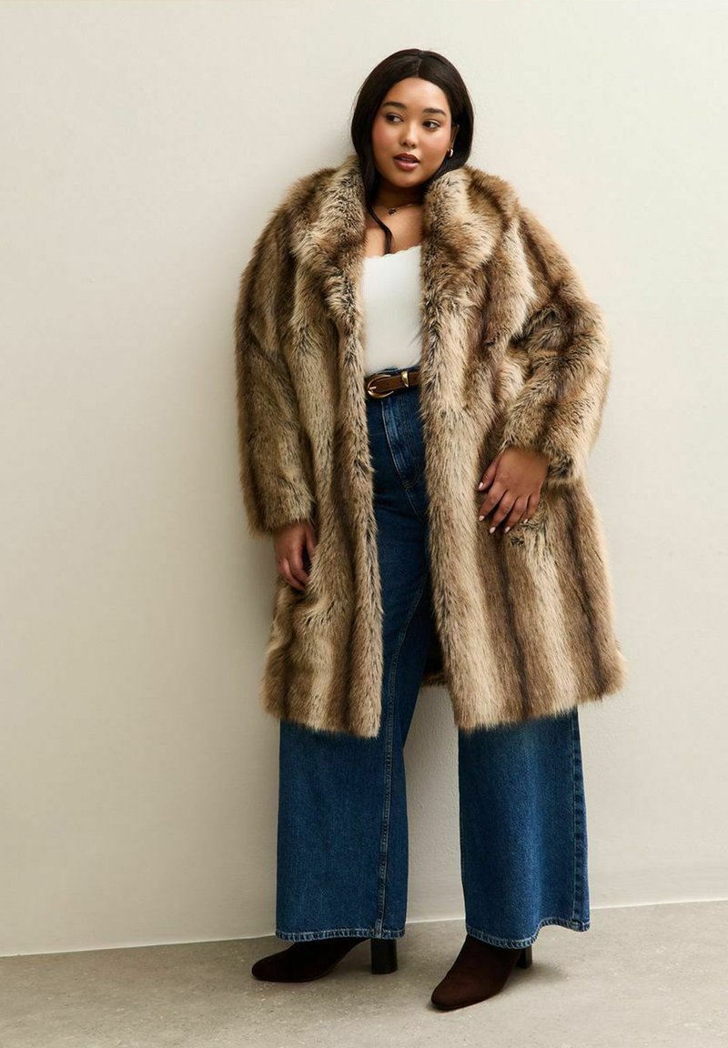 Faux-Fur-Mantel in braunen und beigen Streifen mit lockerer Passform. Kombiniert mit hoch geschnittenen Schlagjeans und dunklen Ankle Boots.