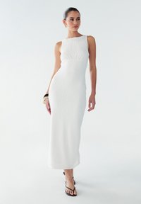 Robe blanche moulante avec un design à côtes texturé. Sans manches avec un col rond, présentant une longueur au genou. Silhouette simple et élégante.