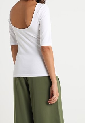 Haut en blanc avec un dos décolleté, des manches mi-longues et une coupe ajustée. Associé à un pantalon large olive. Texture douce.