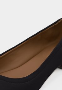 Czarne baleriny z zakrytym noskiem, beżowe wyściełane wnętrze i niski obcas, widoczne pod lekkim kątem z góry.