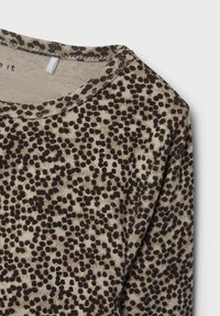 Lange mouw top van beige stof met een bruin stippenpatroon. Ronde halsontwerp met stikseldetails langs de halslijn en mouwen.