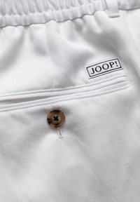 Weiße Stoffshorts mit strukturierter Oberfläche, ausgestattet mit einem Knopfverschluss und einer Gesäßtasche mit einem schwarz-weißen "JOOP!"-Label.