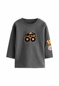 Graues T-Shirt mit kurzen Ärmeln, das auf der Vorderseite einen schwarzen und orangefarbenen Monstertruck-Graphic und ein kreisförmiges Logo am rechten Ärmel hat.