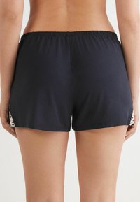 Svarta badshorts med elastisk midja, med ett dekorativt mönster på sidorna. Slät textur och avslappnad passform.