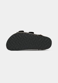 Black rubber footwear sole with a textured diamond pattern, featuring two adjustable straps and a rounded shape.