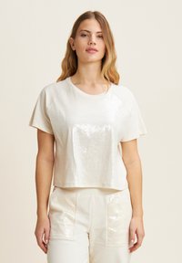 Top blanco de manga corta con un frente de lentejuelas brillantes y un corte holgado. Presenta un escote redondo y una textura de tela suave.