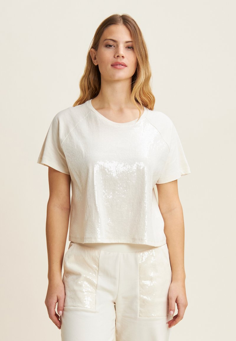 Top blanco de manga corta con un frente de lentejuelas brillantes y un corte holgado. Presenta un escote redondo y una textura de tela suave.