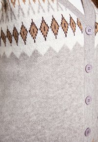 Cardigan lavorato a maglia grigio chiaro con un motivo a rombi bianco e marrone. Presenta una texture sottile e bottoni viola chiaro.