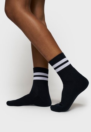 Calze nere alla caviglia con accenti a righe bianche sulla parte superiore. Texture a coste e forma aderente. Adatte per un abbigliamento informale.