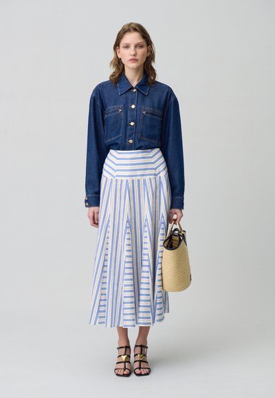 Camisa de mezclilla con botones dorados y dos bolsillos. Falda de rayas plisada en blanco, azul y amarillo. Sandalias negras con tiras y bolso de mimbre.