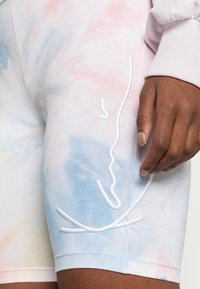 Shorts multicolores courts dans des teintes pastel de rose, bleu et blanc, ornés d'une broderie blanche texturée d'un design minimaliste sur le côté.