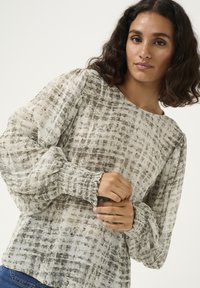 Blouse légère à motif beige et gris avec une coupe décontractée, un col rond et des poignets froncés. Tissu texturé avec un design abstrait.
