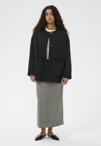 Črna prešita jakna z okroglim izrezom, dvema sprednjima žepoma in zapiranjem na gumbe, kombinirana s sivo črtasto maksi krilo in črni mule čevlji.