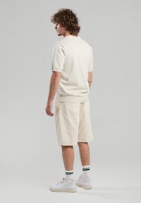 Cream short-sleeve polo and beige cargo shorts. Smooth cotton fabric; shorts feature pockets. Worn with white sneakers and green-striped socks.