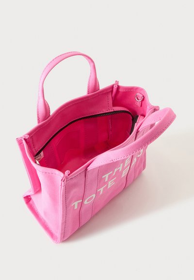 Sac cabas en tissu rose vif avec deux poignées, fermeture éclair partiellement ouverte et texte blanc à l'avant indiquant "THE TOTE BAG."
