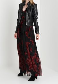 Czarna skórzana kurtka bomber z teksturą prążkowaną, noszona na długiej, plisowanej czarnej sukience z czerwonym wzorem kwiatowym. Całość dopełniają czarne botki za kostkę.