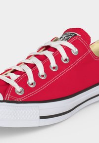 Baskets basses rouges Converse avec lacets blancs, semelle en caoutchouc blanche et détail d'une bande noire, vues de côté et de dessus.