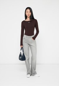 Camiseta burdeos de manga larga, pantalones de mezclilla gris de cintura alta y acampanados, zapatillas blancas y un bolso azul oscuro con herrajes plateados. Diseño texturizado simple.