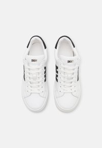 Hvite sneakers med svarte aksentstriper, med en glatt læroverdel, rund tå, flate lisser og DKNY-logo på tungen.