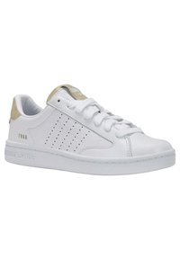 White sneaker with perforated side design, beige accents on heel and tongue, and textured rubber sole. Laces and branding label visible.
