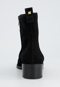 Botas de tobillo de ante negro con punta redonda, cierre de cremallera y tacón bajo tipo bloque. Detalle del logo en dorado en la parte trasera.