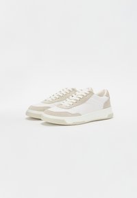 Sneakers con una combinazione di camoscio beige e pelle bianca, caratterizzati da una punta arrotondata, lacci frontali e una spessa suola in gomma crema.