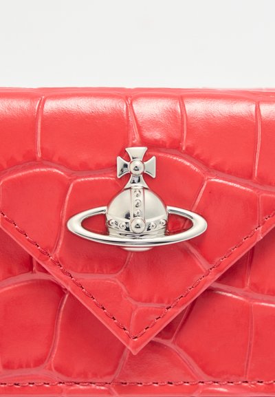 Κόκκινο πορτοφόλι από δέρμα με υφή κροκοδείλου, με ασημί διακοσμητικό σε σχήμα πλανήτη Κρόνου με σταυρό στην κορυφή.