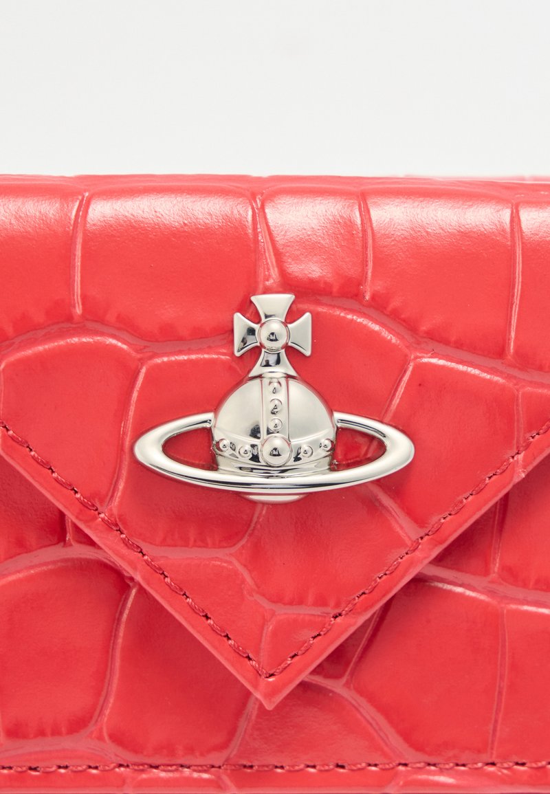 Rotes Portemonnaie aus Leder mit Krokodilprägung und silbernem Ornament in Form eines Planeten Saturn mit einem Kreuz oben drauf.