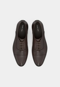 Barna bőrcipő sima felülettel, lekerekített orral és hét fűzőszemmel. Finom kupakorrú kialakítással és lapos talppal rendelkezik.