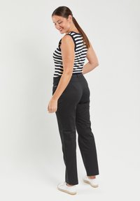 Pantalones negros con cintura elástica, combinados con una blusa sin mangas a rayas azul marino y blanca. Presenta una textura suave y un diseño casual.