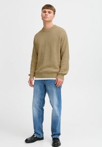 Beige ribbed knit sweater paired with light blue straight-leg jeans. Model wears black leather shoes; the outfit features a casual design.