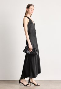 Čierne večerné šaty s hlbokým V-výstrihom, vyrobené z hladkej látky. V kombinácii s čiernym psaníčkom a sandálmi na vysokom opätku s mašľami.