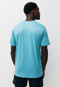 Camiseta deportiva azul claro con tejido texturizado, escote redondeado y mangas cortas, con un sutil detalle de costura en la parte trasera.