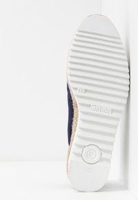 Semelle en caoutchouc blanc d'une chaussure Gabor taille 41,5, montrant un motif d'adhérence texturé et l'inscription « Fabriqué en Slovaquie », inclinée contre une surface blanche.