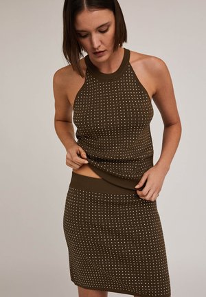 Haut en tricot sans manches marron à pois blancs, avec col montant et coupe ajustée, associé à une jupe coordonnée arrivant au genou.
