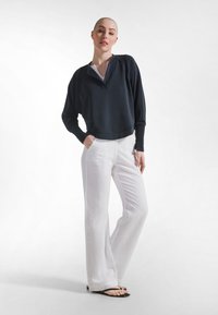 Tummansininen collegepaita napillisella kauluksella, yhdistetty leveälahkeisiin valkoisiin housuihin ja mustiin varvassandaaleihin. Sileä kangas ja rento istuvuus.