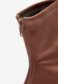 Gros plan sur la partie supérieure d'une botte en cuir marron montrant une fermeture éclair latérale et une couture en zigzag le long du bord supérieur.