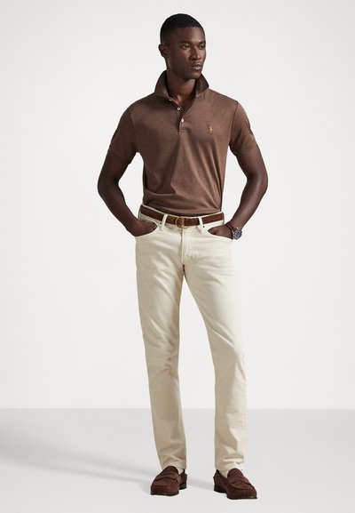 Camisola polo castanha com colarinho, combinada com calças beje claras. Cinto castanho e sapatos castanhos casuais completam o visual. Design simples e clássico.