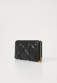 Carteira de couro preta com superfície acolchoada, fecho de zíper dourado e forma retangular, apresentando um design texturizado e acabamentos lisos.