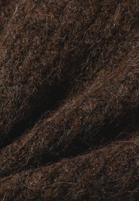 Nahaufnahme von dunkelbraunem, flauschig strukturiertem Wollstoff, der weiche, dicke Fasern und ein gemütliches Strickmuster zeigt.