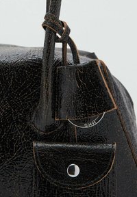 Acercamiento a un bolso de cuero negro texturizado con correa, anilla para llaves adjunta y pequeño bolsillo con botón a presión.