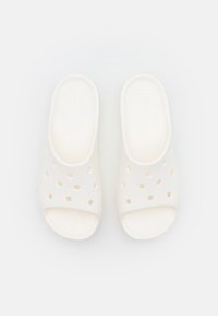 Ett par vita gummisandaler utan snörning med ventilationshål, texturerad fotbädd och öppen tå, placerade mot en enkel ljus bakgrund.