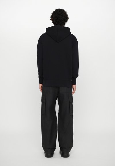 Felpa con cappuccio nera in cotone, dal design semplice e con polsini a costine. Indossata con pantaloni cargo neri larghi dotati di tasche laterali.