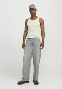 Jeans oversize gris clair, débardeur côtelé blanc cassé et casquette lavande/mauve avec le texte "GLENDALE". Des bottes à cheville marron complètent l'ensemble.