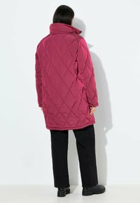 Giacca a vento trapuntata magenta con cuciture diagonali, colletto alto e maniche lunghe. Abbinata a pantaloni neri e stivali neri robusti.
