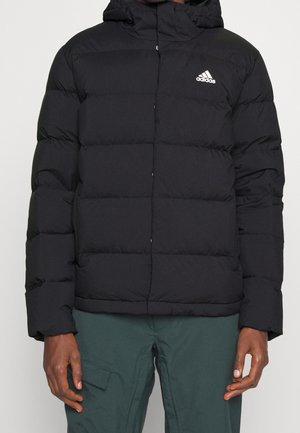 Personne portant une doudoune à capuche noire Adidas avec un logo visible, associée à un pantalon cargo vert foncé.