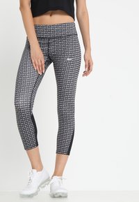 Czarno-białe legginsy capri z powtarzającym się wzorem "Just do it". Tkanina odprowadzająca wilgoć o dopasowanym kroju. Połączone z białymi butami sportowymi.
