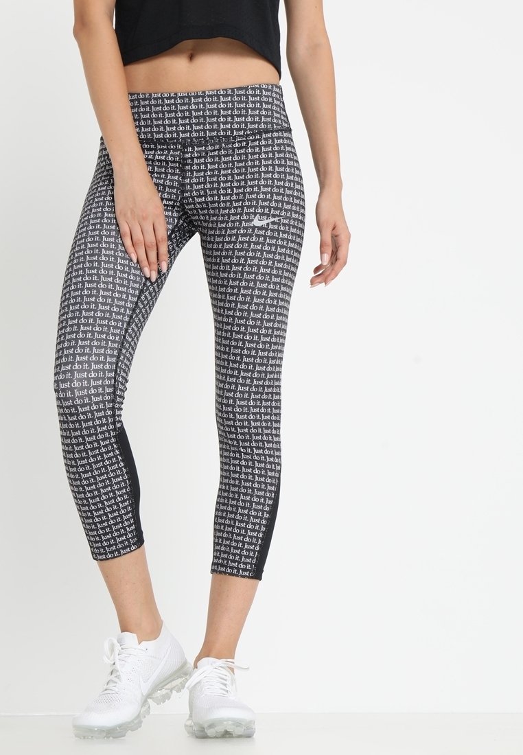 Černobílé capri legíny s opakujícím se vzorem textu "Just do it". Materiál odvádějící vlhkost s přiléhavým střihem. Doplnené bílými sportovními botami.
