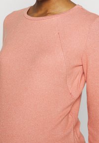 Světle růžové tričko s dlouhým rukávem z měkké tkaniny s kulatým výstřihem, s bočními švy a jemným strukturovaným povrchem.